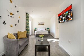 A modern hotel room with a grey sofa, a bed with a white duvet, a black coffee table, and a wall-mounted TV displaying a Netflix interface. - For Your most relaxed and cosy stay (West Yorkshire)