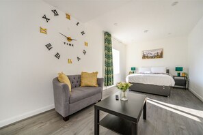 A modern hotel room with a grey sofa, a bed, a wall clock, and a painting on the wall. - For Your most relaxed and cosy stay (West Yorkshire)