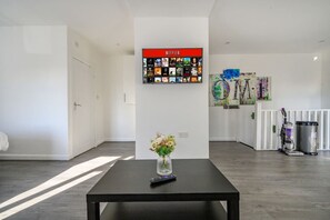 A modern living room with a black table, a vase with flowers, a wall-mounted Netflix display, and a colorful abstract painting. - *11F2* Captivating & luxurious Stay (West Yorkshire)
