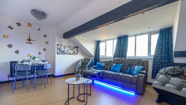 Un soggiorno moderno con un divano, poltrone massaggianti, una zona pranzo con sedie e un soffitto decorato con orologi.