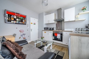 Um apartamento moderno com sala de estar, cozinha compacta e tela para Netflix na parede.