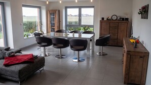 Un salon moderne avec un coin repas, de grandes fenêtres et une vue sur l’extérieur.