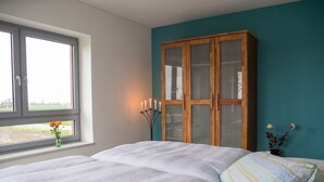 Une chambre à coucher avec un lit, une fenêtre, une armoire en bois et un vase rempli de fleurs.