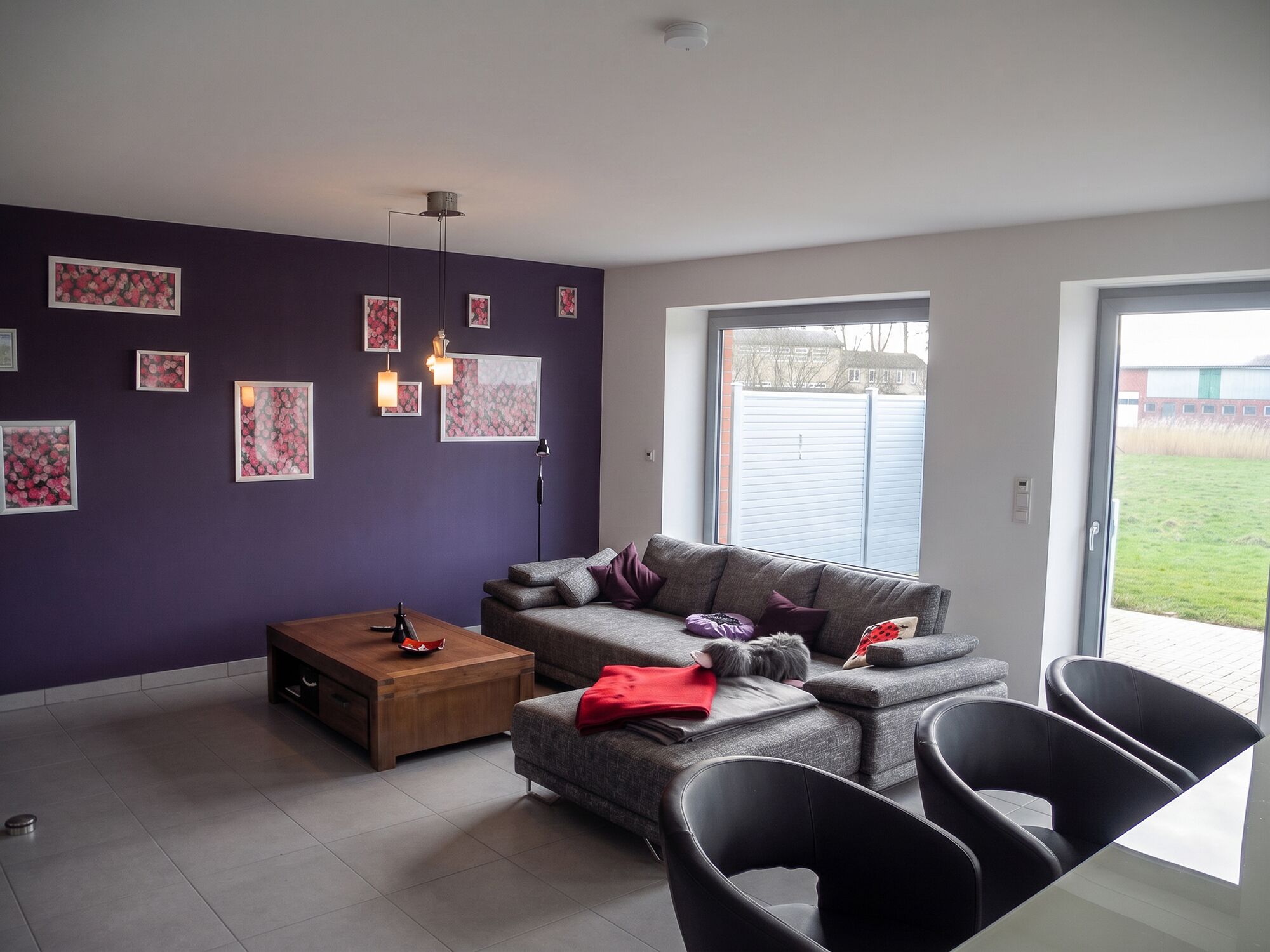 A modern living room with a sofa, coffee table, and chairs, a large window, and artwork on the walls.