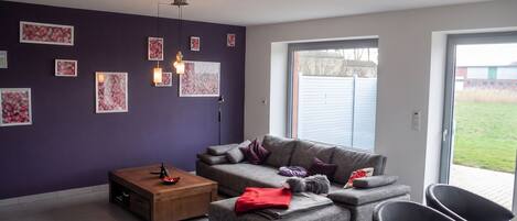 A modern living room with a sofa, coffee table, and chairs, a large window, and artwork on the walls.