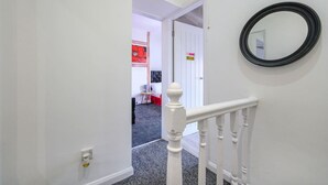 A hallway with a white railing, a black-framed mirror, and a door leading to a room with a red flower painting.