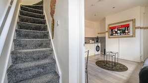 A staircase leading to a living area with a kitchen, a washing machine, and a wall-mounted Netflix display.