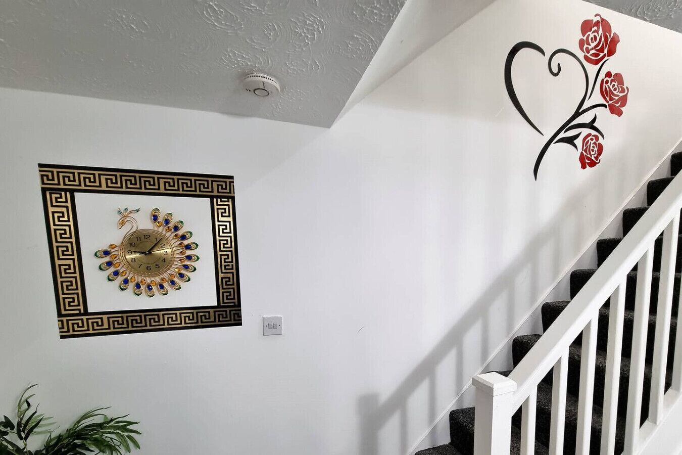 A staircase with a white railing, a decorative wall clock, and a wall art piece with red roses.