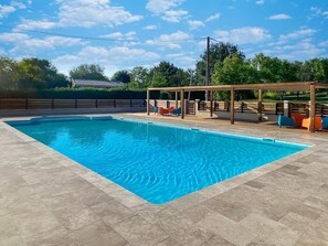 Une piscine rectangulaire avec une terrasse carrelée, entourée d’une pergola en bois agrémentée de chaises.