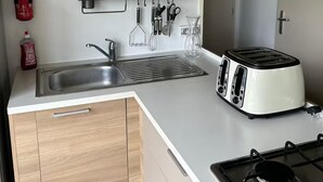 Cocina compacta con pileta, tostadora, cocina a gas, alacenas de madera y extintor.