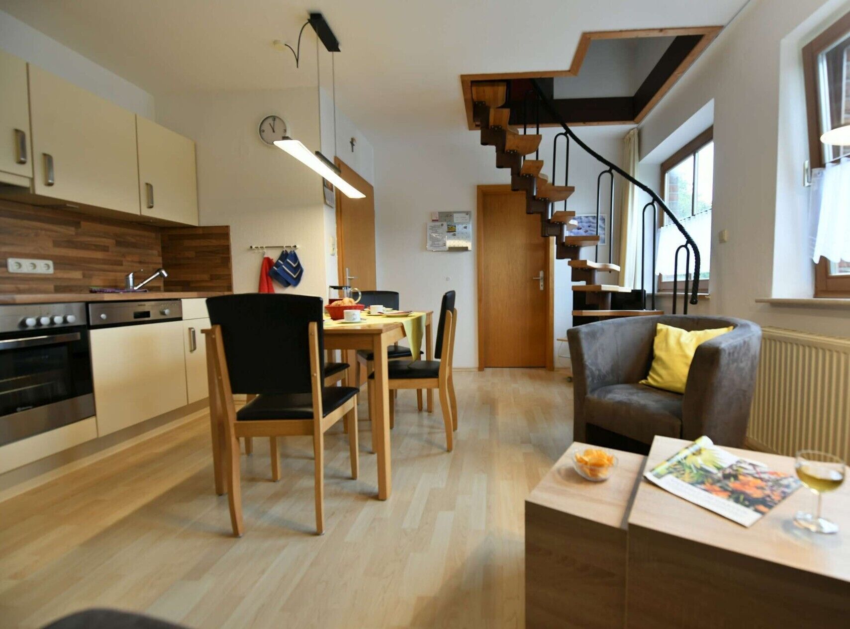 Eine moderne Küche mit Holzschränken, ein Essbereich mit Tisch und Stühlen, ein Sofa und eine Treppe mit außergewöhnlichem Design.