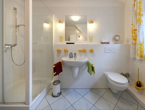 Ein Badezimmer mit Duschkabine, Waschbecken mit Spiegel darüber, Toilette und Mülleimer.