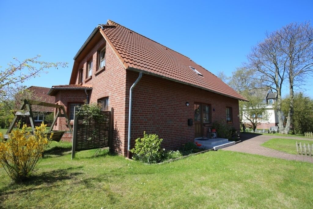 Ein rotes Backsteinhaus mit geneigtem Dach, einer Veranda und einem kleinen Garten.
