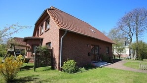 Ett hus byggt av rött tegel med ett sluttande tak, en veranda och en liten trädgård.