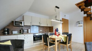 Ett modernt kök med mikrovågsugn, brödrost och kaffebryggare, ett matbord med stolar och en sovplats på ett loft.