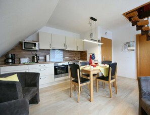 Eine moderne Küche mit Mikrowelle, Toaster und Kaffeemaschine, ein Esstisch mit Stühlen sowie eine erhöhte Schlafkoje.