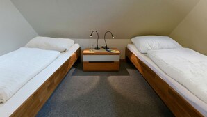 Ett litet, enkelt rum med två separata sängar, ett träbord vid sängen med en lampa och ett golv täckt med matta.