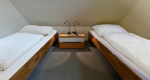 Eine kleine, einfache Unterkunft mit zwei Einzelbetten, einem Nachttisch aus Holz mit Lampe und Teppichboden.