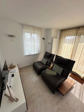 Ein modernes Wohnzimmer mit einer Couch, einem kleinen Tisch, einem Fernseher und einem Fenster mit Vorhängen.