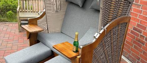 Un espacio exterior con asientos de mimbre, un banco acolchado y una pequeña mesa de madera, junto a una botella de champán.