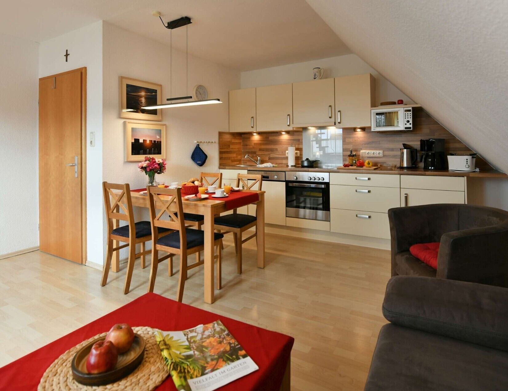 Eine moderne Küche mit Holzausstattung, einer Mikrowelle und einer Kaffeemaschine. Es gibt eine Essecke mit einem Tisch für zwei Personen und eine Couch in der Ecke.