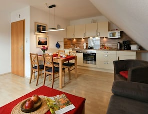 Eine moderne Küche mit Holzausstattung, einer Mikrowelle und einer Kaffeemaschine. Es gibt eine Essecke mit einem Tisch für zwei Personen und eine Couch in der Ecke.