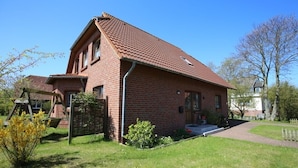 Ein rotes Backsteinhaus mit geneigtem Dach, einer Veranda und einem kleinen Garten.