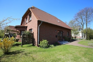 Ein rotes Backsteinhaus mit geneigtem Dach, einer Veranda und einem kleinen Garten.