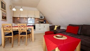Ein kompakter Wohnbereich mit Essplatz, Küchenzeile und einer Couch mit roten Kissen.