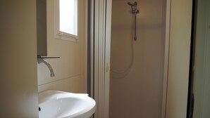 A bathroom with a white sink, a shower with a handheld showerhead, and a window above the sink. - 5-person Mobile Home Near Chianti (Bucine)