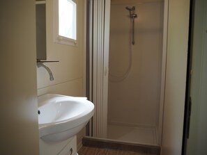 A bathroom with a white sink, a shower with a handheld showerhead, and a window above the sink. - 5-person Mobile Home Near Chianti (Bucine)