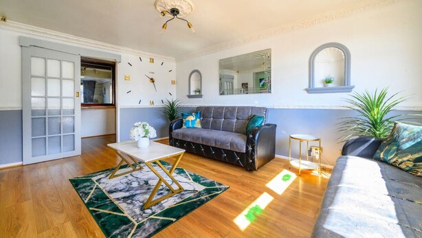 A living room with a sofa, a coffee table, a clock, a mirror, and a plant. - Stylish Home with Hot Tub in Hawksworth (Hawksworth)
