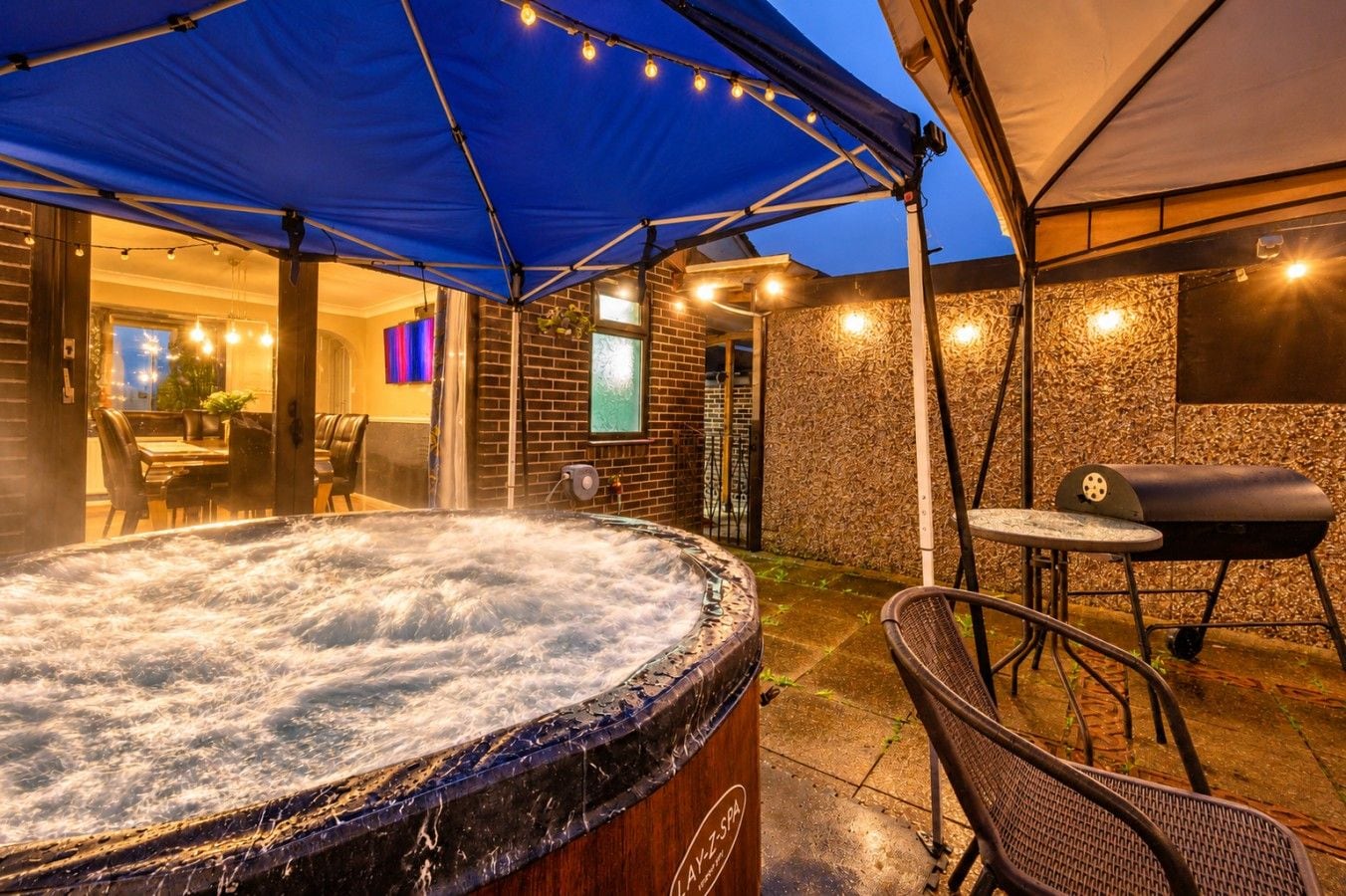 Ein Whirlpool unter einer blauen Markise, mit Grill und Sitzgelegenheit.
