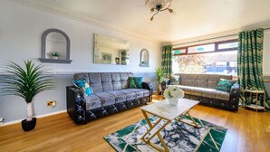 A living room with a sofa, a coffee table, and two potted plants. - Stylish Home with Hot Tub in Hawksworth (Hawksworth)