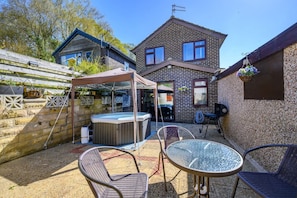 Un jardin avec un jacuzzi, des chaises de patio, une table en verre et une maison en briques.
