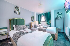 Ein Hotelzimmer mit zwei Betten, einem Flachbildfernseher, einer Chandelüster und Kunstwerken an den Wänden.
