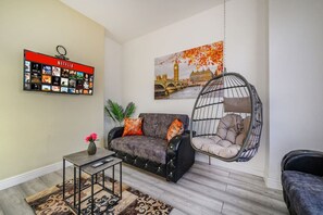 A living room with a sofa, a hanging chair, a coffee table, a TV wall art, and a framed picture of a cityscape.