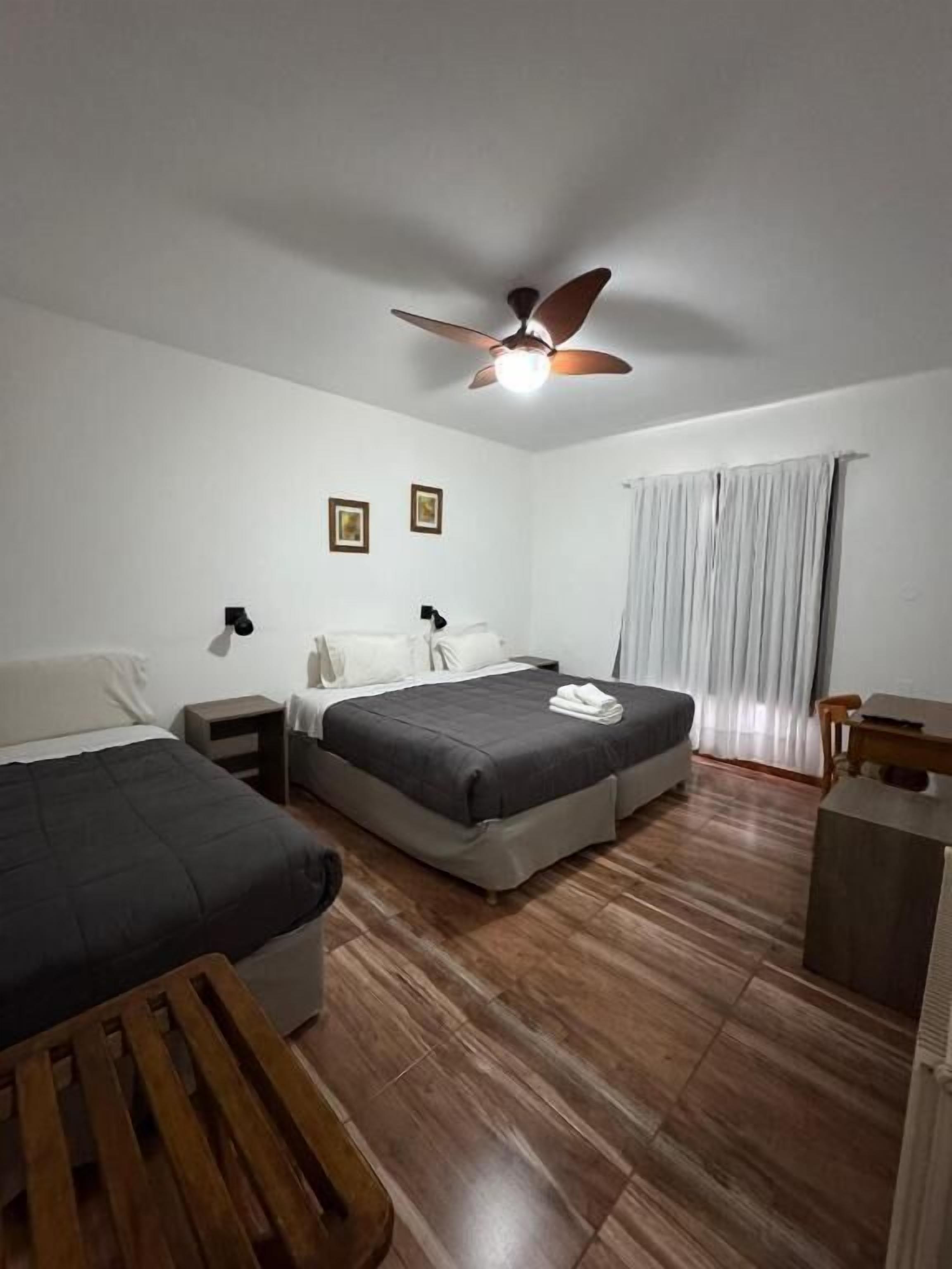 A bedroom with two beds, a ceiling fan, a nightstand, a wooden bench, and a desk.