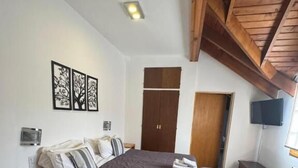 A bedroom with a bed, wooden flooring, a ceiling fan, a TV, and a door. - Hosteria Cumbres Blancas (Esquel)