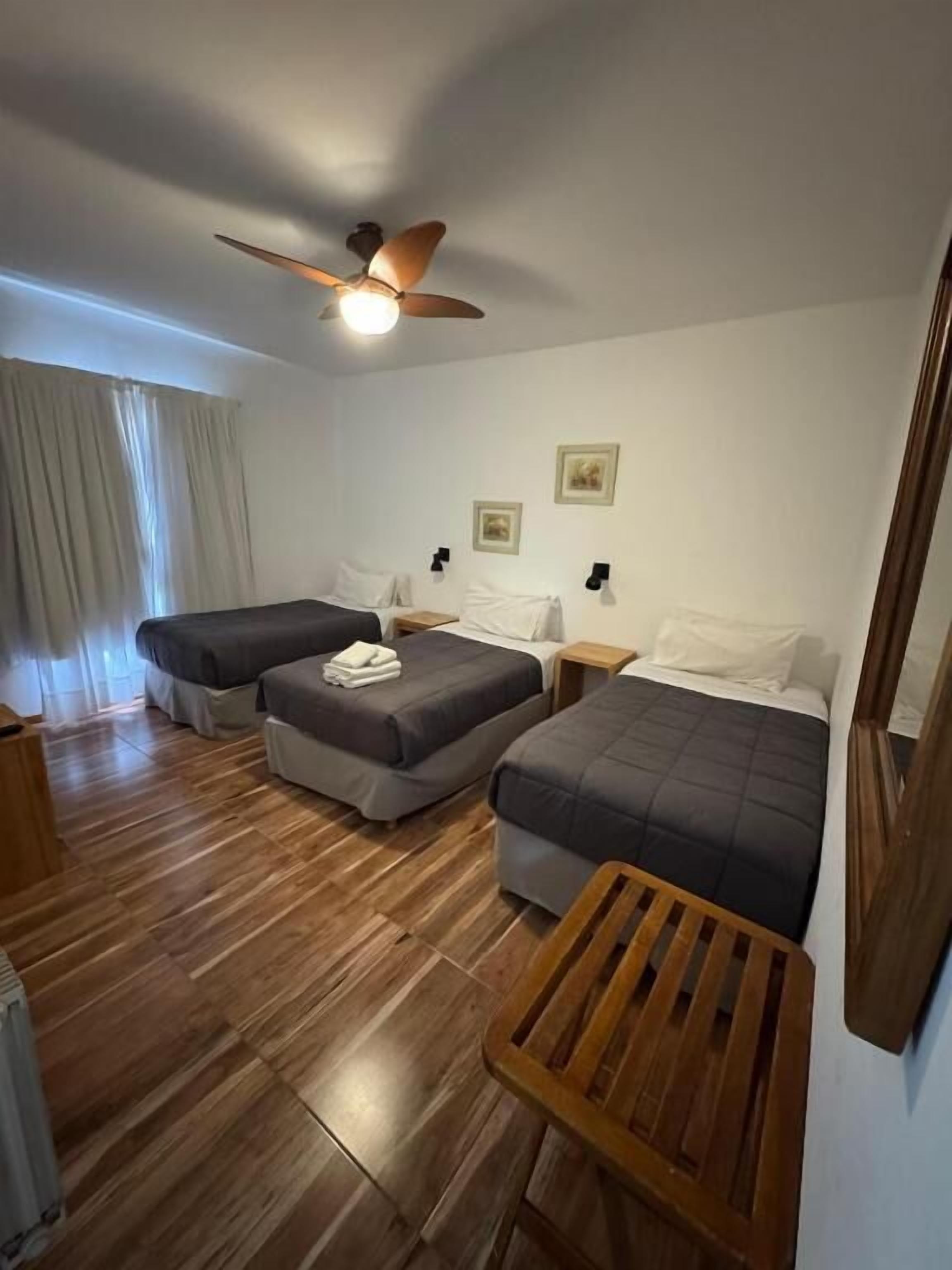 A hotel room with two beds, a ceiling fan, wooden flooring, and a small wooden table.