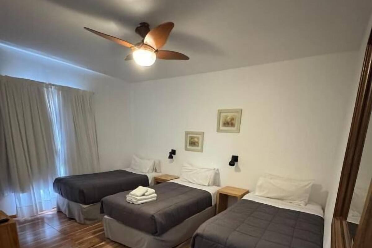Habitación de hotel con dos camas, ventilador de techo, piso de madera y una pequeña mesa de madera.