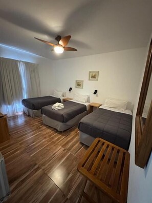 A hotel room with two beds, a ceiling fan, wooden flooring, and a small wooden table. - Hosteria Cumbres Blancas (Esquel)