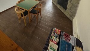 A living room with a stone fireplace, a dining area with a green table and chairs, and a view of the outdoors through large windows. - Hosteria Cumbres Blancas (Esquel)