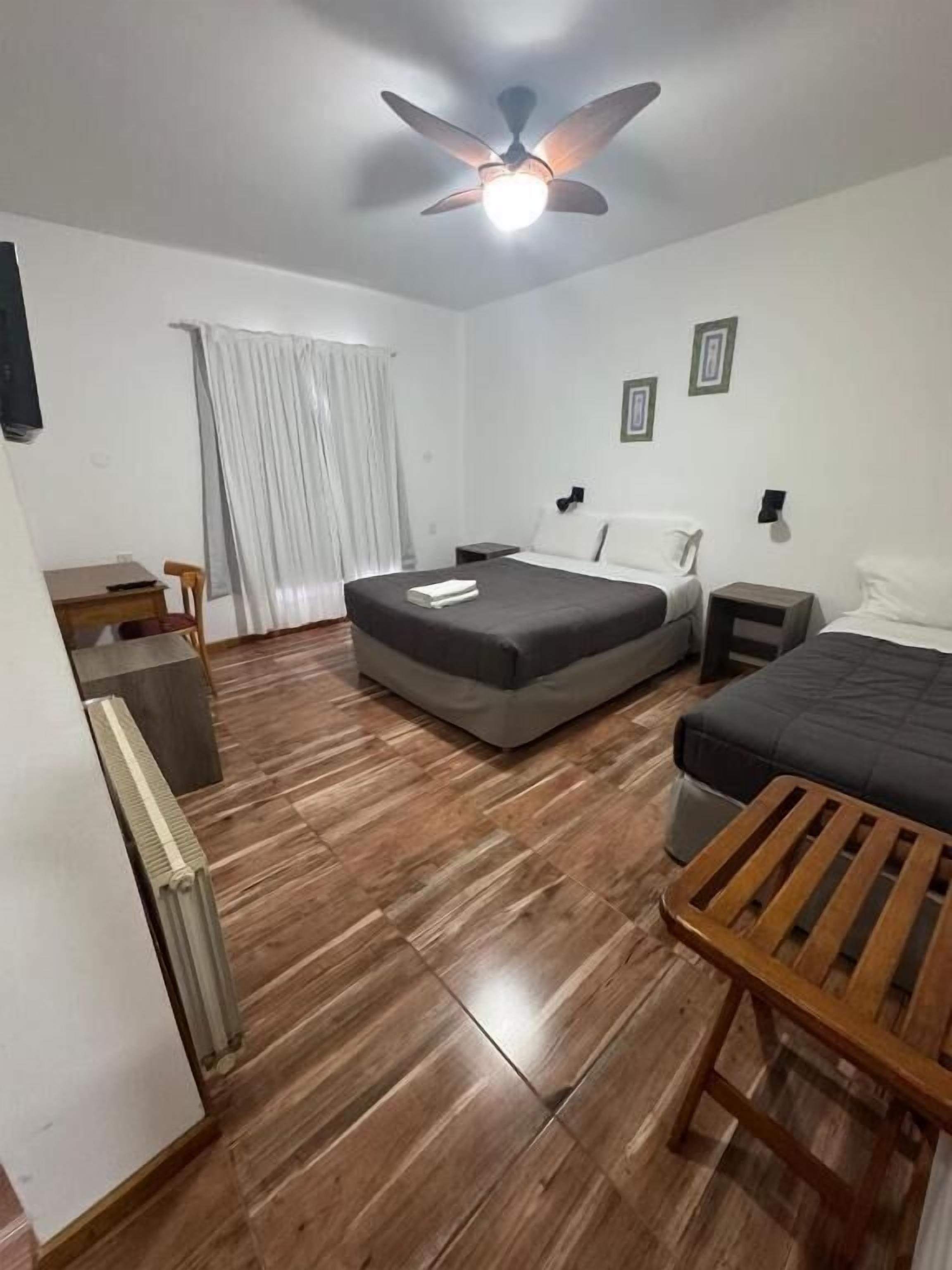 A room with a bed, a desk, a chair, a ceiling fan, and a radiator.