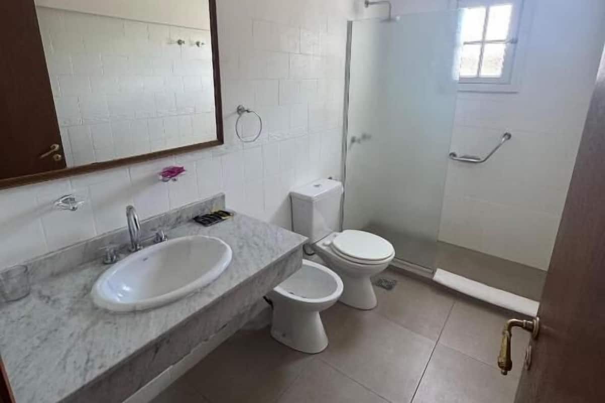 Un baño con lavamanos de mármol, dos inodoros, una ducha y un ventanal pequeño.