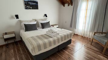 A bedroom with a wooden ceiling, a bed with striped bedding, a nightstand, a chair, and a window with curtains.