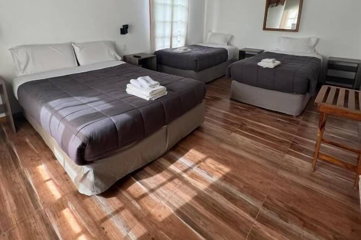 Una habitación con dos camas, ventilador de techo, espejo y piso de madera.
