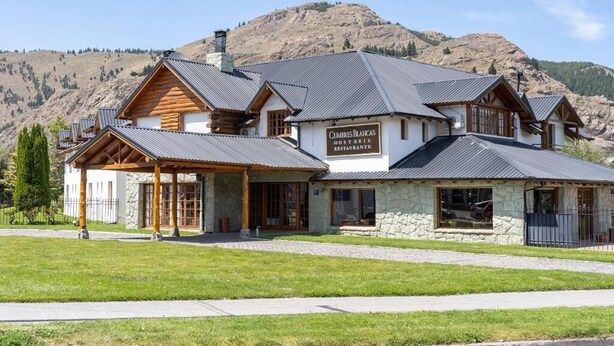 A mountain lodge with a stone facade, wooden beams, and a sign reading 'Cumbres Blancas Restaurante.' - Hosteria Cumbres Blancas (Esquel)