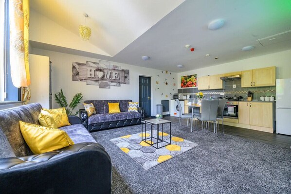 A modern living room with a sofa, a coffee table, and a kitchen area with cabinets and appliances.