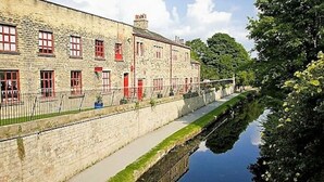 A stone building with red doors and windows, a canal beside it, and a fence. - Stylish Ground Floor Apartment in West Yorkshire (West Yorkshire)
